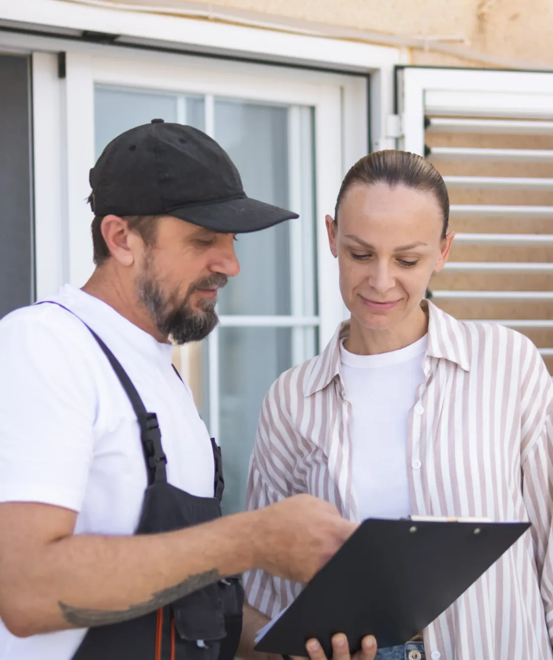 A contractor reviewing a written estimate on a clipboard with a homeowner outside her house