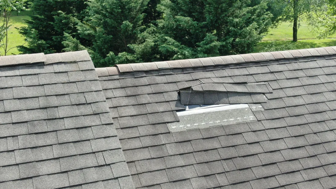 A shingle roof section with a missing shingle and exposed decking, a visible damage sign