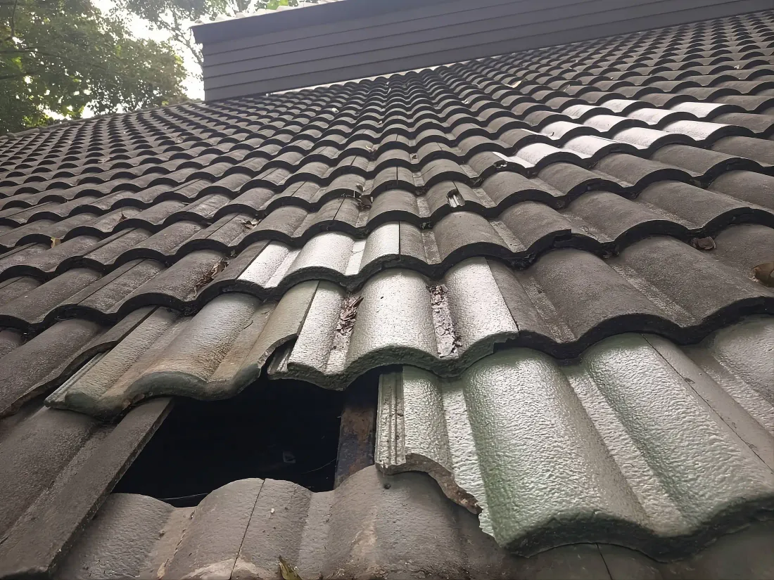 A cracked and broken clay roof tile with a visible hole, the kind of localized tile damage a repair quote typically covers